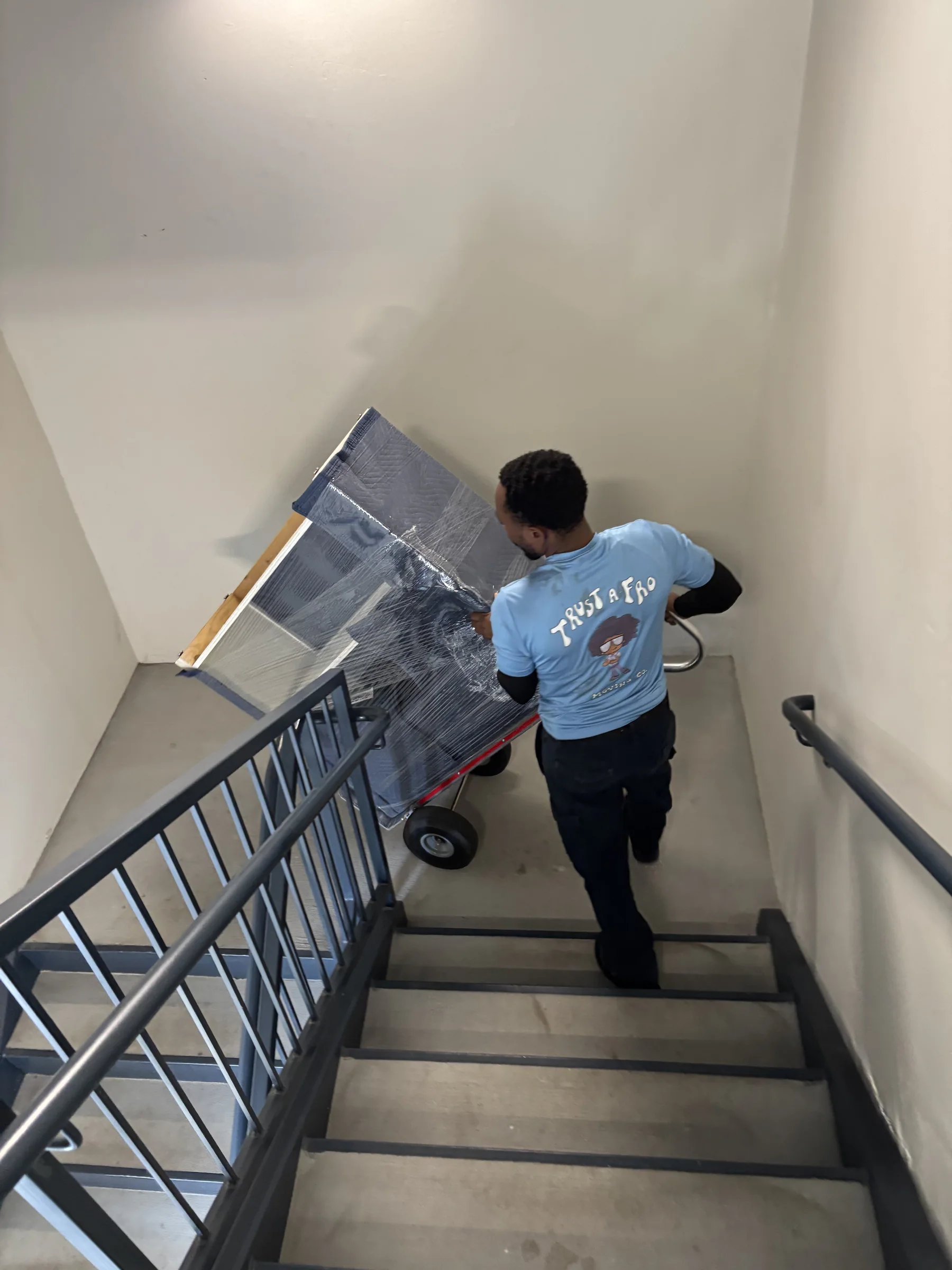 A Trust A Fro mover taking a wrapped piece of furniture down a stairwell on a hand truck