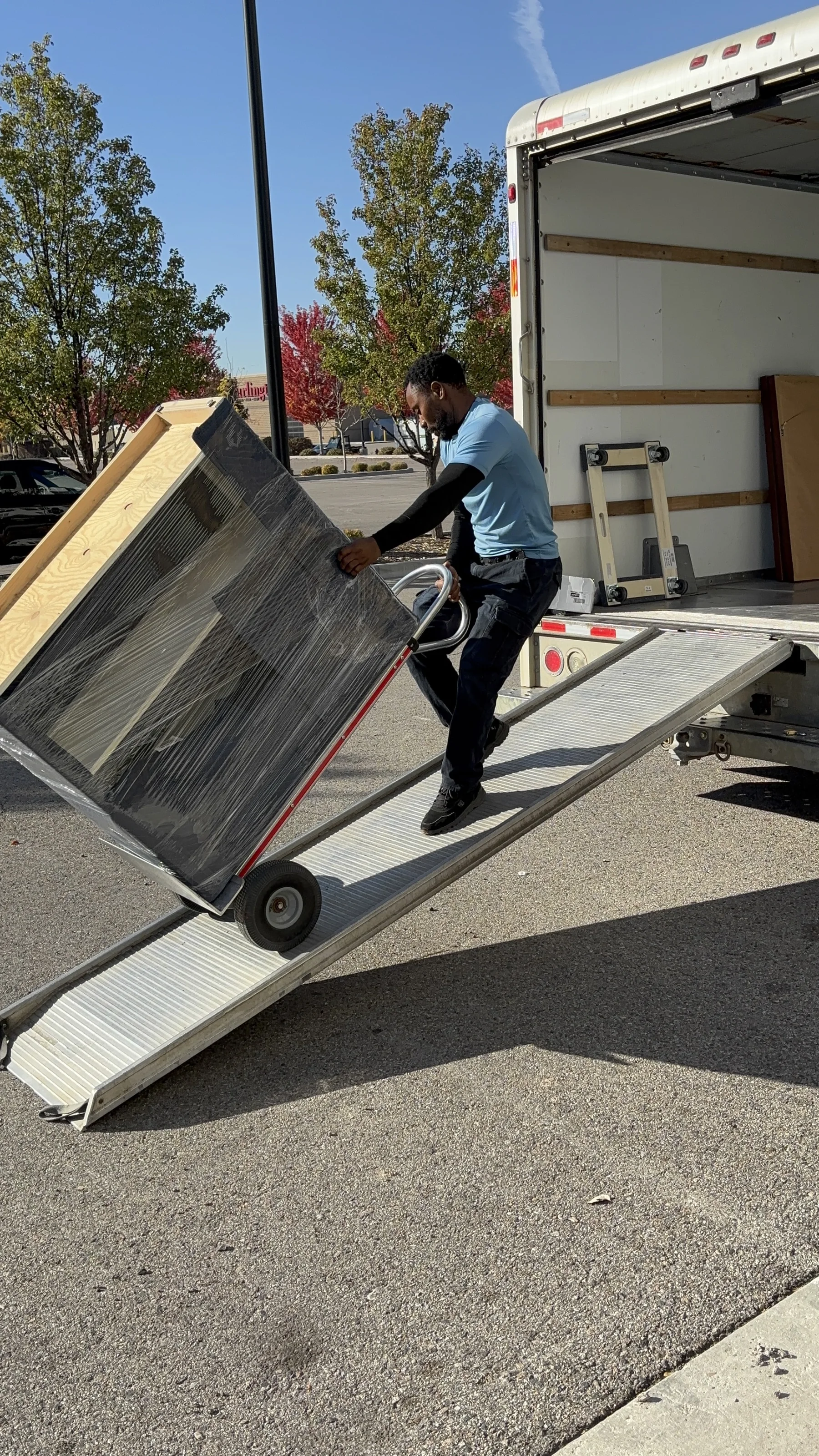 A mover wheeling wrapped furniture up the ramp into the truck